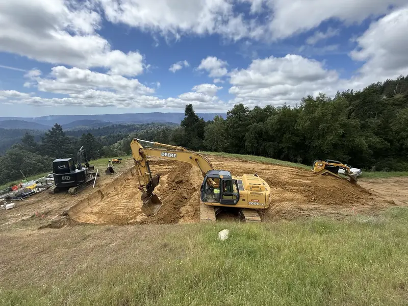Excavator cutting a building pad into a grassy ridge with valley views
