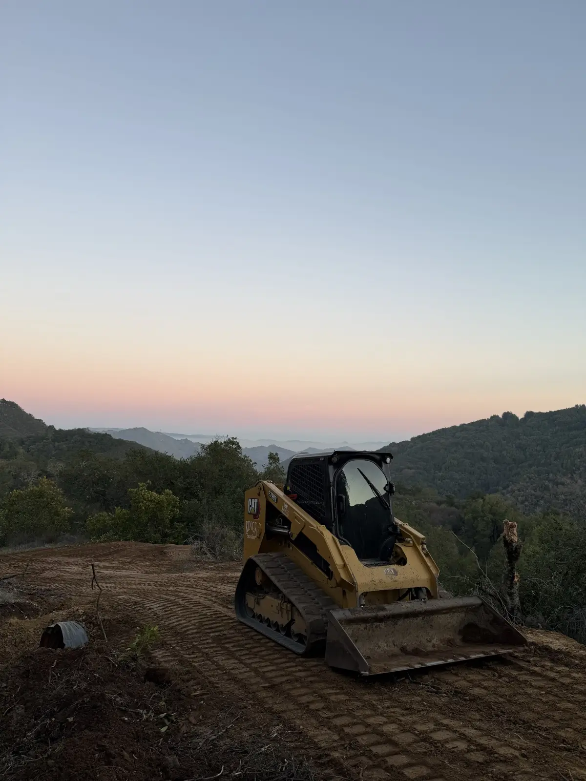 Skid steer on a freshly cleared and graded ridgetop at sunset