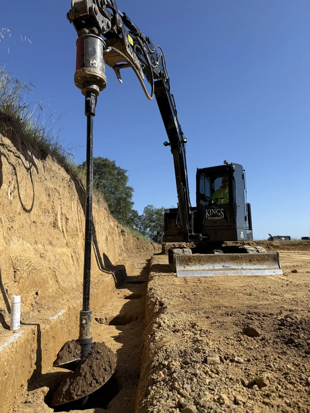 Excavator drilling a pier hole for a foundation on a sloped site