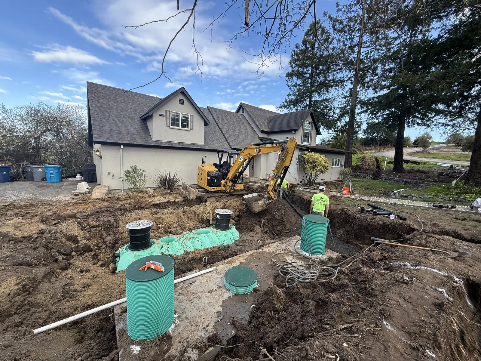 Residential septic system installation with green tank risers, a Kings crew, and the home behind